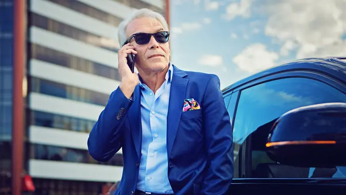 Businessman is talking using his mobile phone standing next to his car.