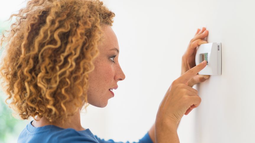 25-29 Years, Blonde Hair, Curly Hair, Day, Differential Focus, Head And Shoulders, Horizontal, Indoors, Latin American and Hispanic Ethnicity, Mixed Race Person, New Jersey, One Person, One Young Woman Only, Side View, Smiling, Technology, Temperature, Touching, USA, Wall, adjusting, african american ethnicity, air conditioning, close up, heating, home, jersey city, pressing, setting, thermostat, woman