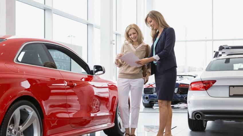 Saleswoman showing woman brochure in car dealership showroom.