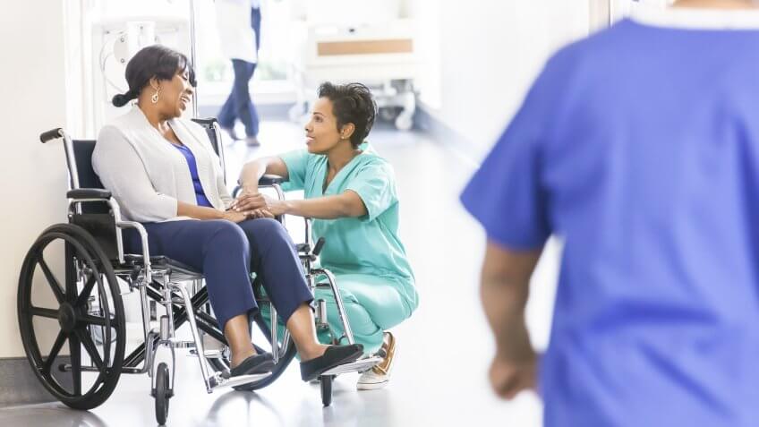 African American female patient in hospital wheelchair in corridor specialist care unit with medical staff.