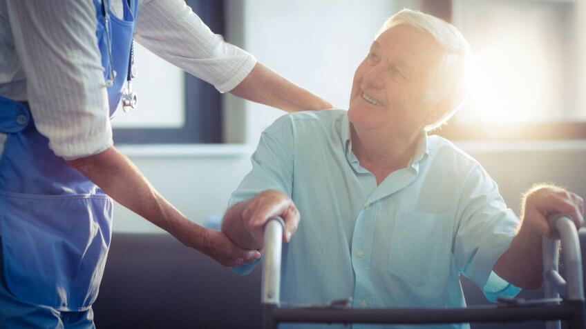 Female doctor helping senior man to walk with walker at home.