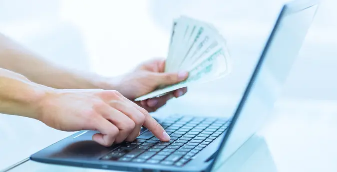 hands holding cash typing on computer