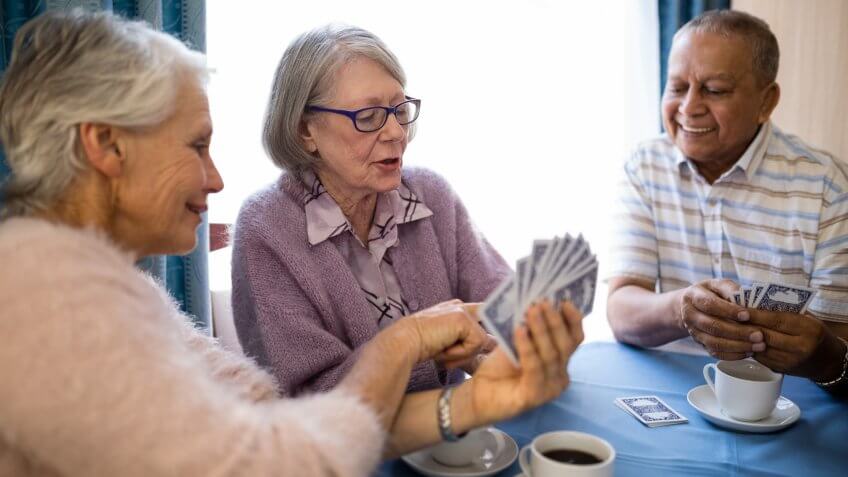 Smiling senior woman showing cards to friends while playing at table in nursing home.