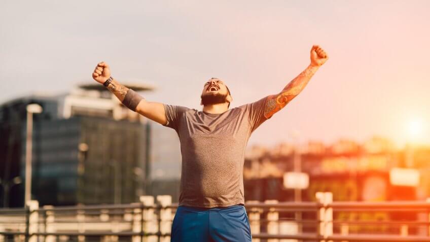 Male Runner Jogging in the city and finishing his training with his hands up in the air screaming with happiness.