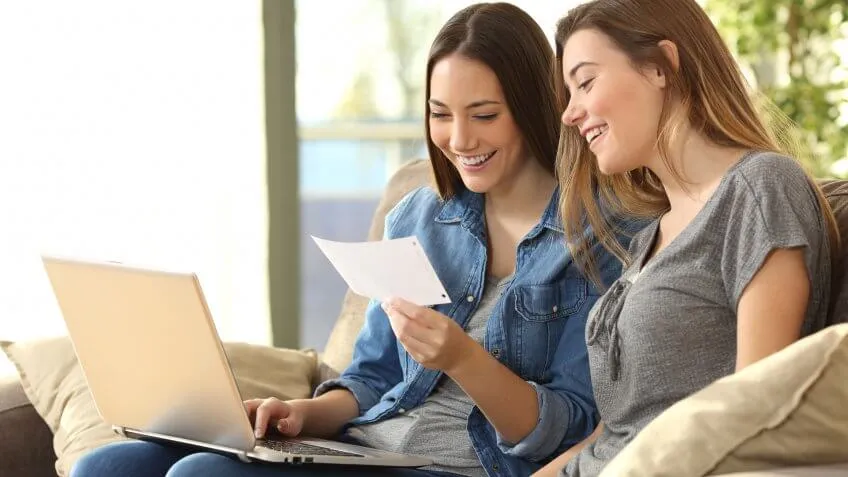 two young women smiling looking at a piece of paper and laptop
