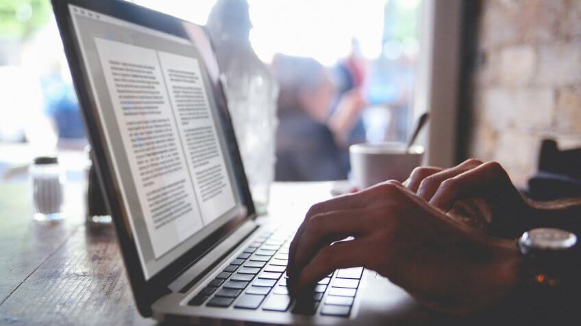 Vintage toned image of man's hands typing on the laptop in the cafe.