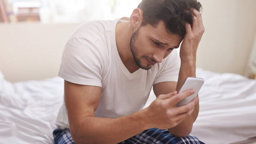 They have a secret bank account. stressed man looking at phone in bed
