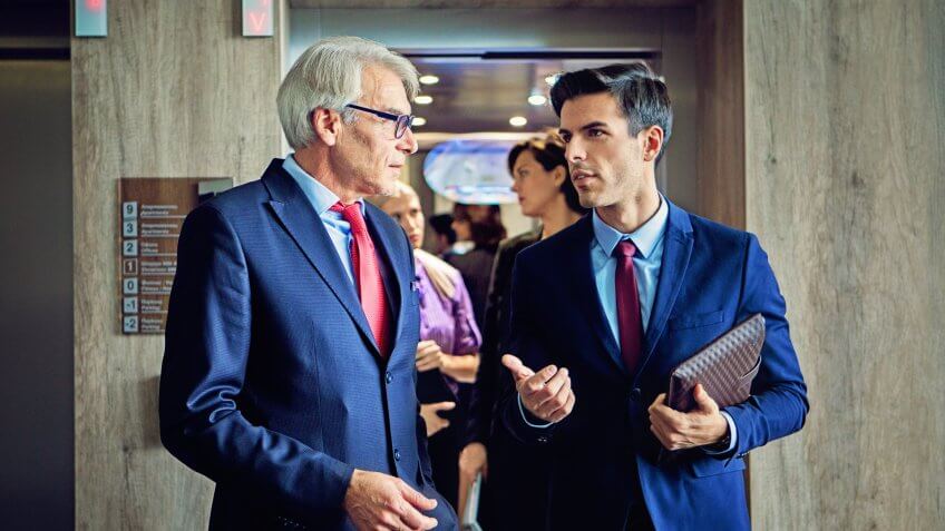 Businessmen are exiting from the elevator in the company building discussing between them.