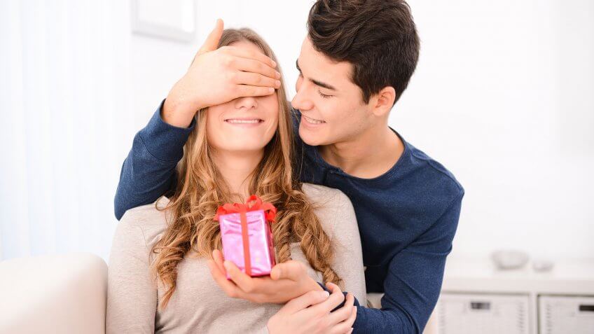 You are trying to buy love. guy with hands over girl's eyes surprising her with a gift