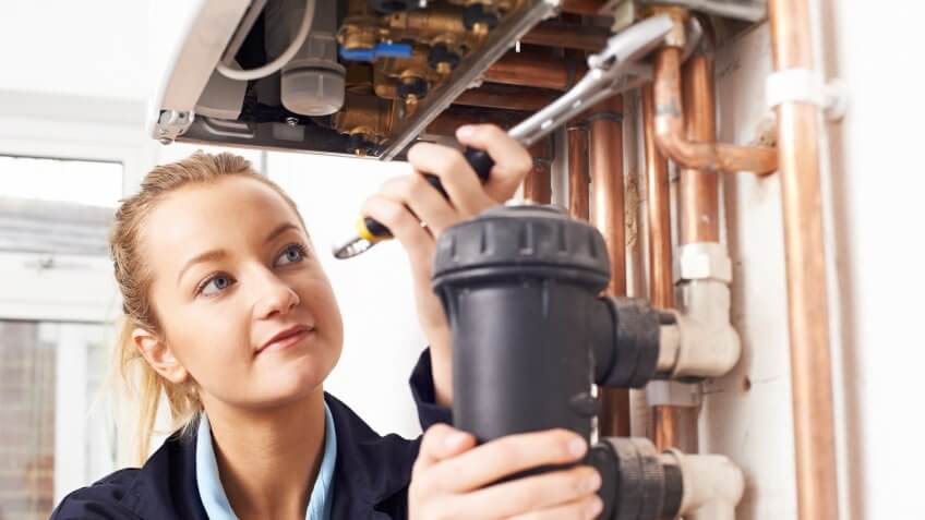 Female Plumber Working On Central Heating Boiler.