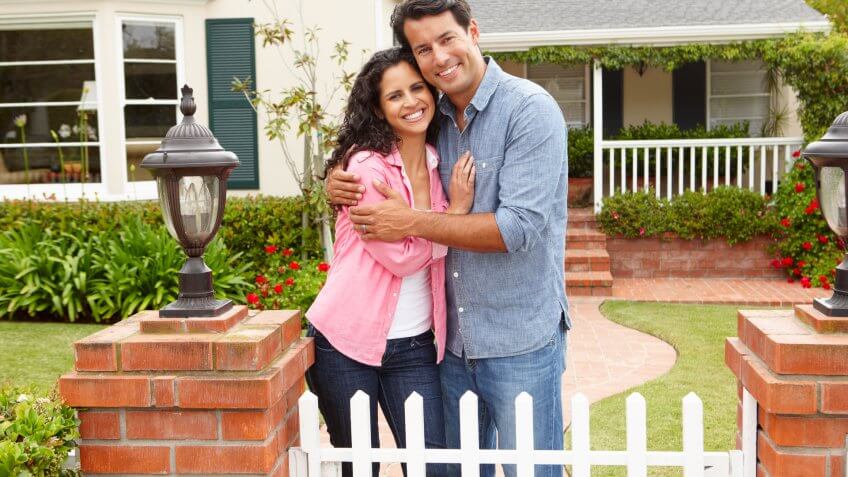 young couple smiling in front of their home