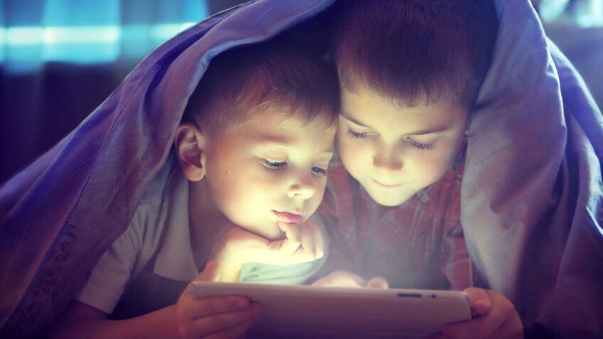 brothers looking at tablet under blanket