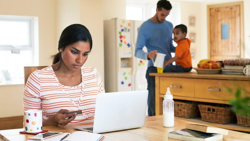 woman holding credit card looking at laptop while man tends to a toddler child in the back