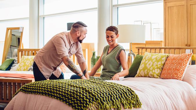 A middle aged couple are shopping in a furniture store for a new bedroom, the customers are both sat on the bed to see how comfortable it is, trying it out.