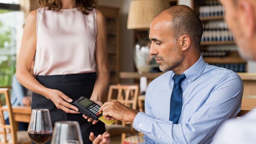 Waiter holding credit card swipe machine while customer typing code.