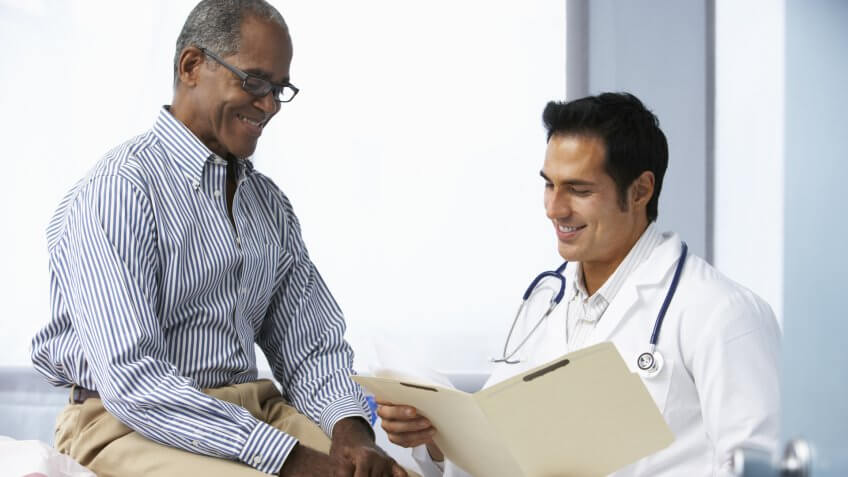Doctor In Surgery With Male Patient Reading Notes.