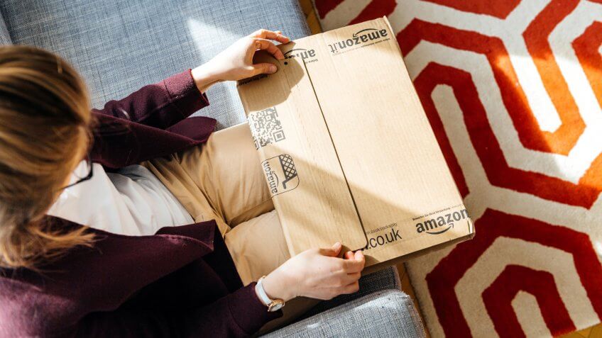 PARIS, FRANCE - APR 24 2017: Living room view from above of woman unpacking unboxing Amazon cardboard box logotype printed cardboard box side.
