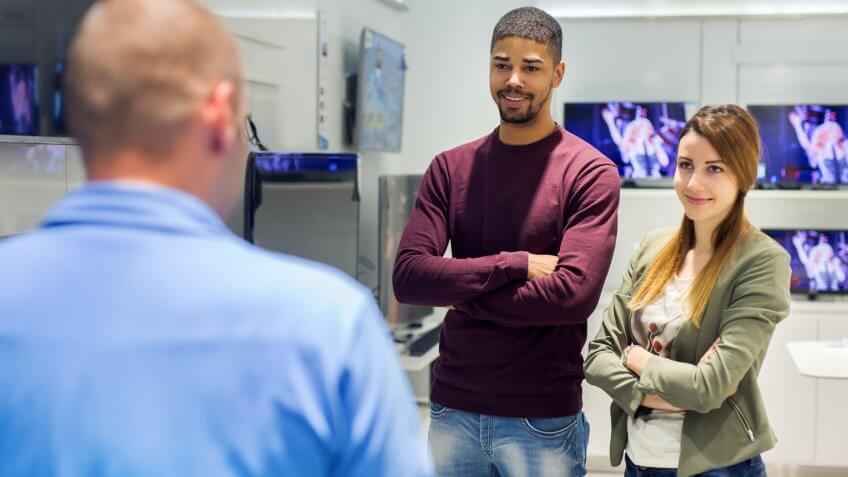 Young couple at tech store looking at seller.