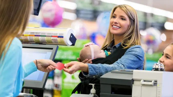 Mid adult Caucasian woman is shopping local grocery store or supermarket with elementary age daughter and infant.