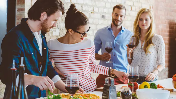Friends cooking together in the modern kitchen, preparing pizza, drinking wine.