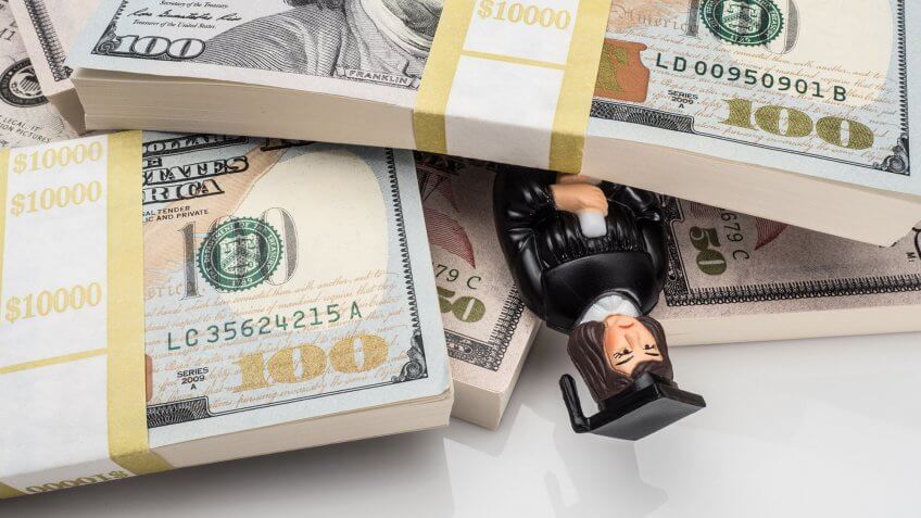 Many students find themselves on the wrong side of things when it comes to loans. graduate figurine buried under stacks of cash