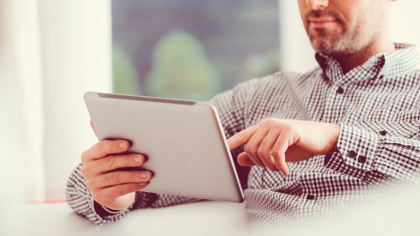 Handsome man wearing glasses and shirt using a digital tablet at home.