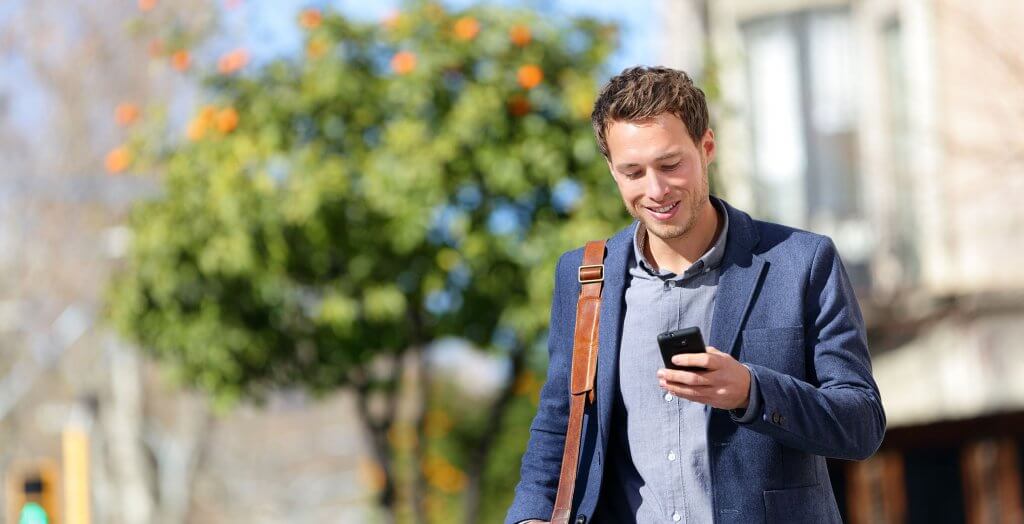 Banking technology increases accessibility and affordability. man walking looking at phone tree in background