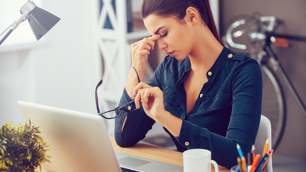Borrowing money from loved ones puts financial strain on them. woman taking off glasses frustrated at work