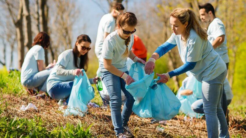 volunteering, charity, cleaning, people and ecology concept - group of happy volunteers with garbage bags cleaning area in park.
