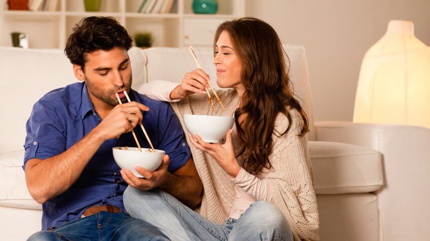 couple eating a bowl of food with chopsticks in their living room
