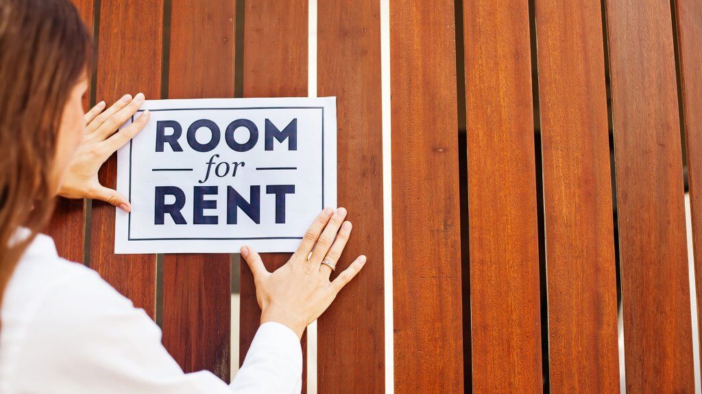 You can rent out your home. woman placing 'room for rent' sign up