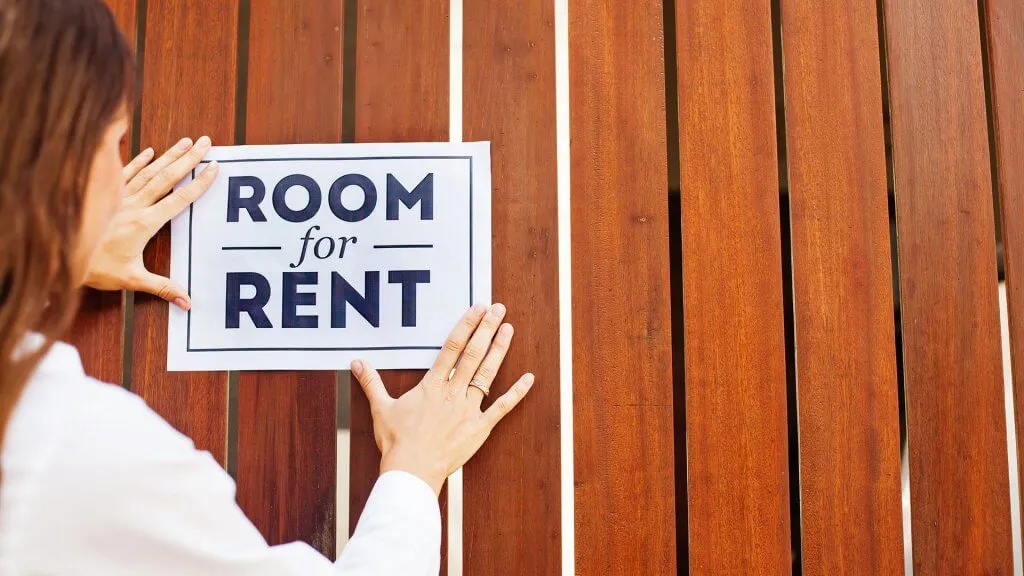 woman placing 'room for rent' sign up