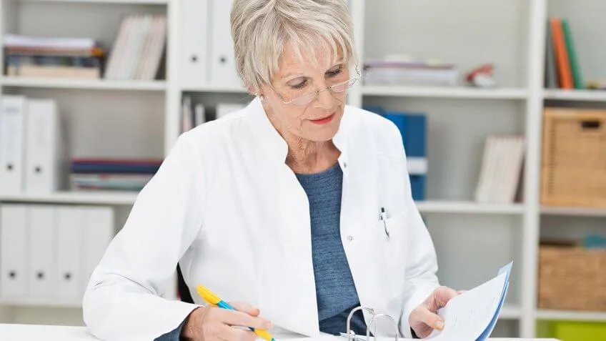 elderly woman in lab coat examining a document