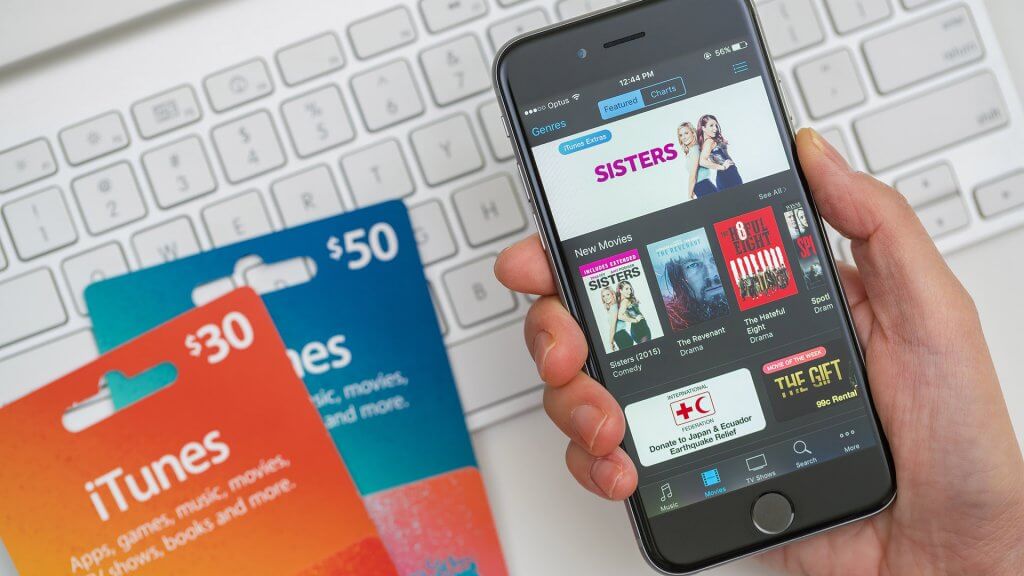 You won't get the best deal on gift cards in November. hand holding iPhone with iTunes gift cards on keyboard