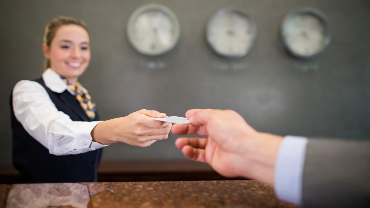 Woman working at a hotel handing a loyalty card or card key at the front desk.