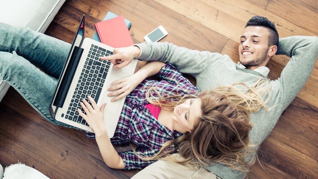 Book your vacation in advance. couple laying on floor and looking on laptop together