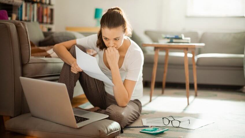 Photo of a young woman sitting on the floor and working on laptop.