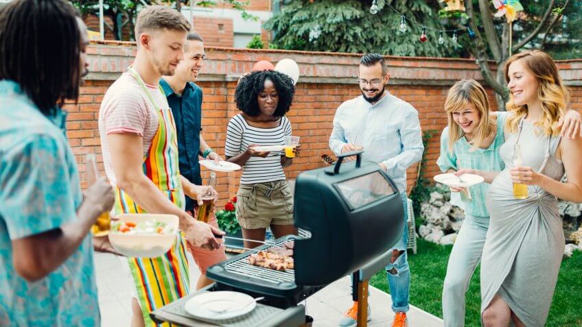 Group of young people eating at barbecue party in a backyard.
