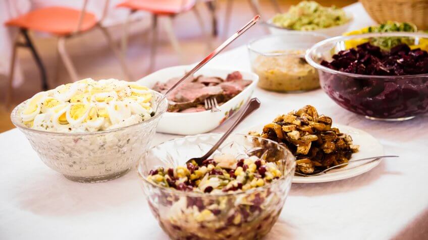 Potluck buffet table with several salad and meat dishes.
