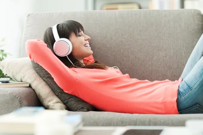 a woman laying on her couch with headphones on.