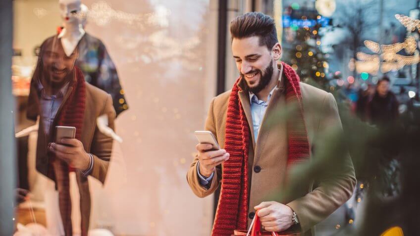 Young man holding Christmas bags and checking his smart phone.