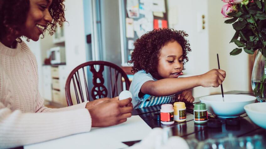 A photo of mother assisting girl in painting Easter egg