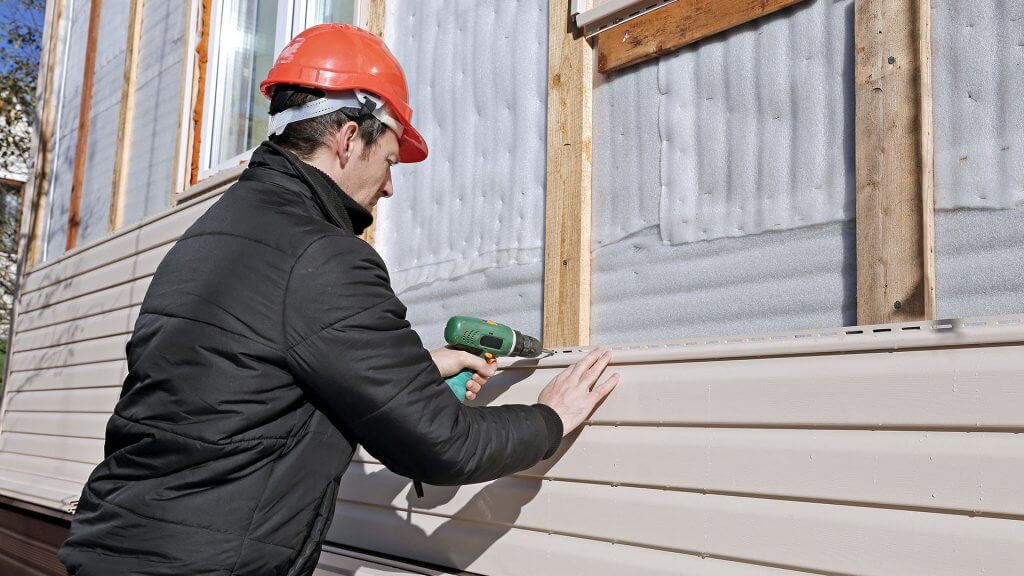 Vinyl siding is expensive, but it is often a good investment. man using power drill on house that's under construction