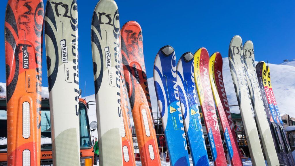 Rental gear is cheaper and more convenient for casual skiers. several pairs of rental skis resting on a rack