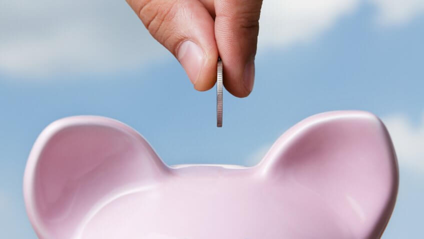 Hand putting a coin into piggy bank.