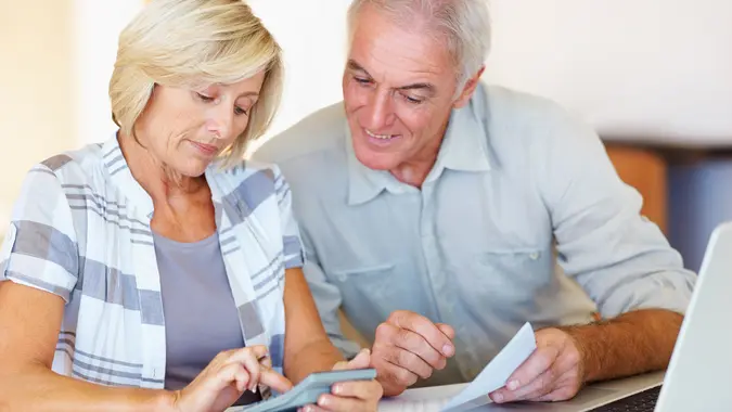Happy senior couple budgeting their monthly expenses using calculator at home
