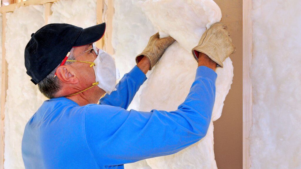 New insulation is a great investment that homeowners should consider. man with facemask on installing insulation