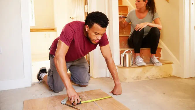 Man and woman working together to renovate a home, painting walls and updating interior features.