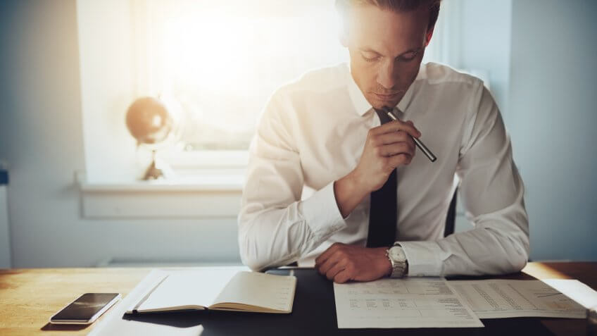 Serious business man working on documents looking concentrated with briefcase and phone on the table.