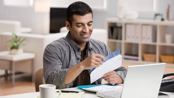 Hispanic man opening mail in home office.